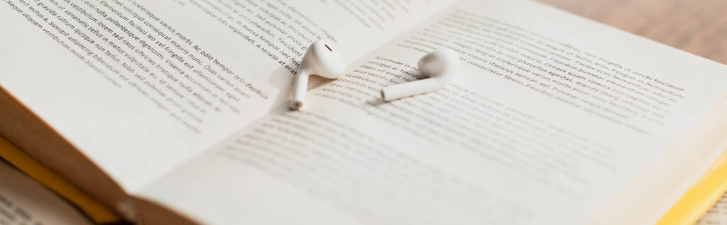 белые беспроводные наушники на размытой книге, баннер - Фото, изображение