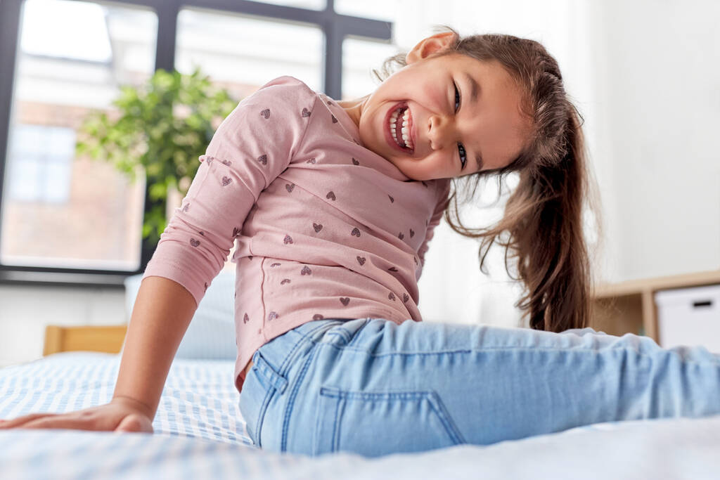 счастливая улыбающаяся маленькая девочка, сидящая дома на кровати - Фото, изображение