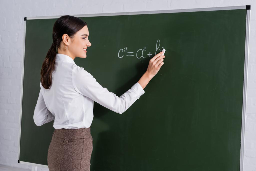 Hymyilevä opettaja kirjoittaa matemaattista yhtälöä liitutaululle  - Valokuva, kuva