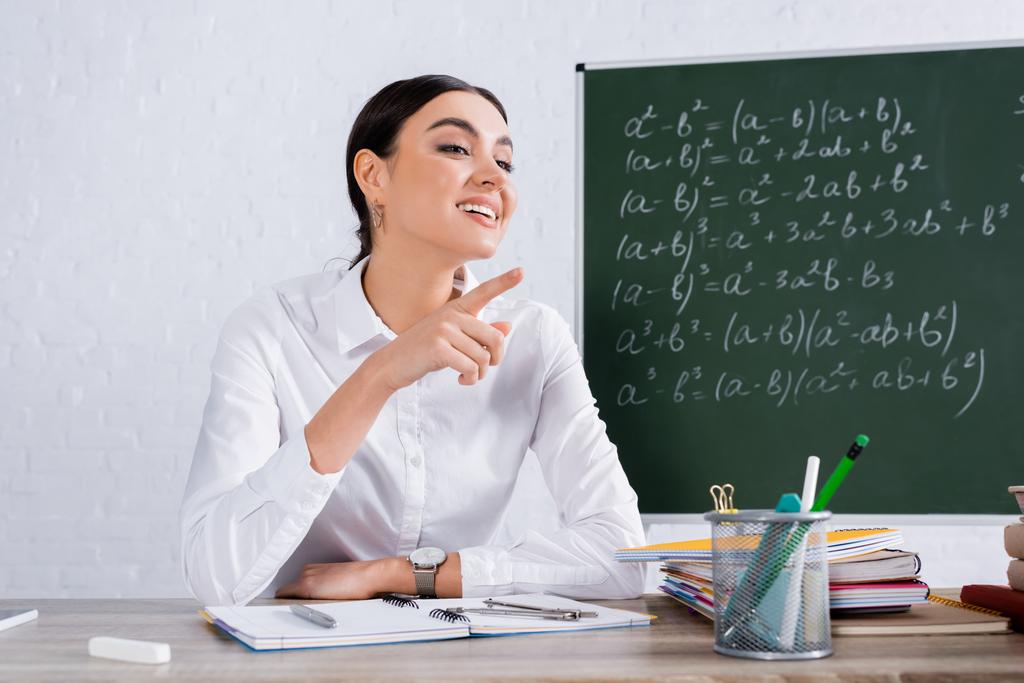 Учитель указывает пальцем на блокноты и размытый мел  - Фото, изображение