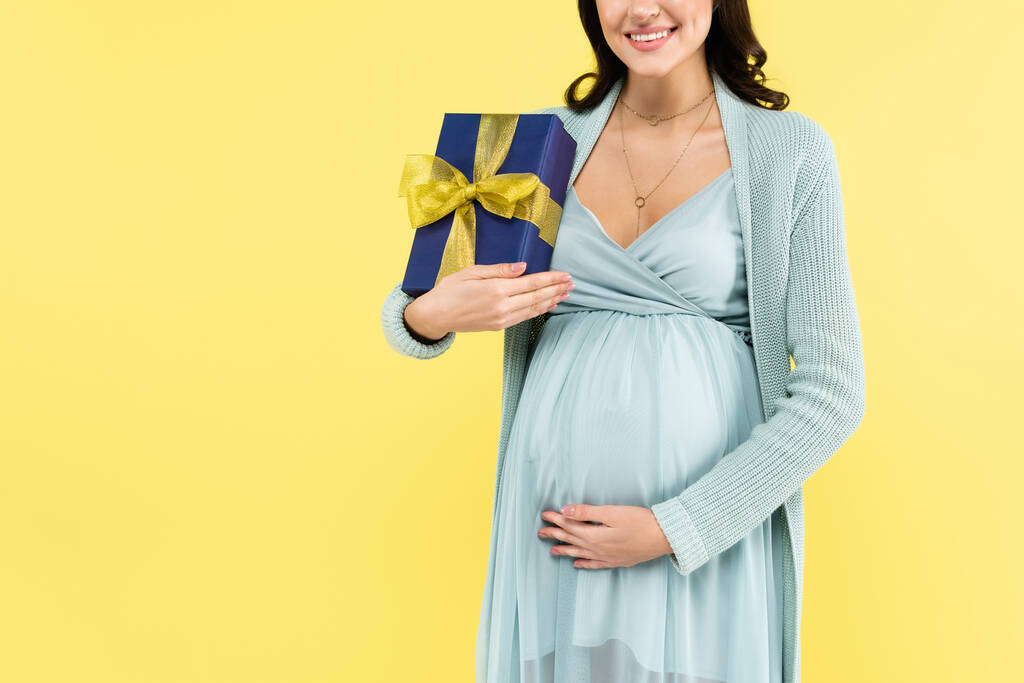 parziale con di donna incinta in possesso di confezione regalo e toccante pancia isolata su giallo - Foto, immagini