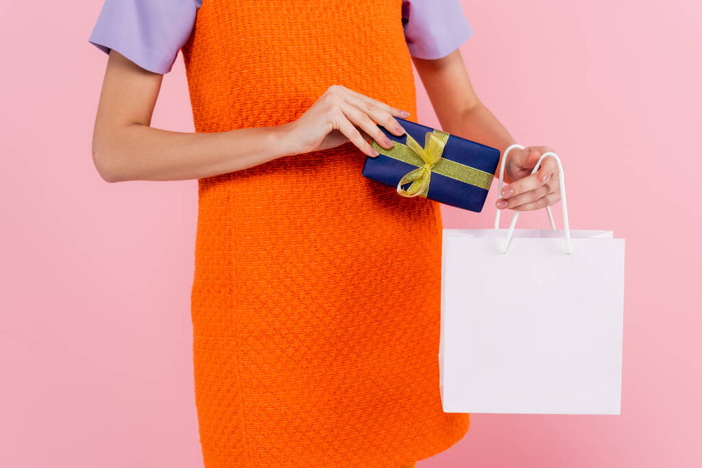 vista parcial de la mujer sosteniendo caja de regalo y bolsa aislada en rosa - Foto, Imagen