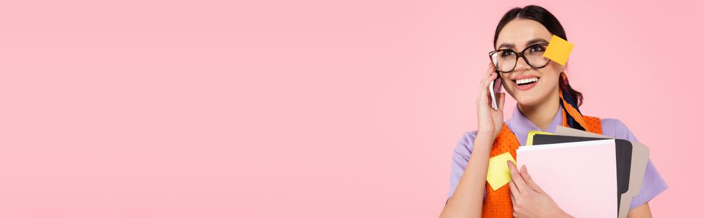 szczęśliwy businesswoman gospodarstwa foldery i rozmowy na telefon komórkowy odizolowany na różowy, baner - Zdjęcie, obraz