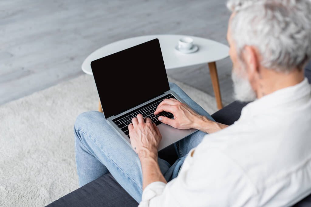 размытый фрилансер с седыми волосами с помощью ноутбука, сидя дома на диване - Фото, изображение