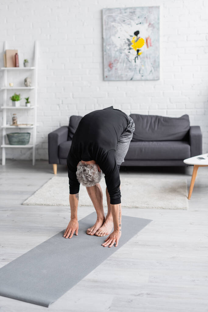 intera lunghezza dell'uomo scalzo che si esercita sul tappeto fitness in soggiorno  - Foto, immagini