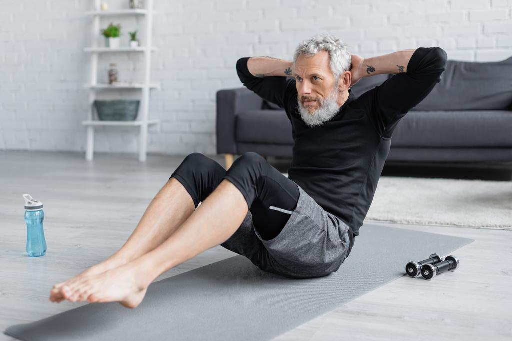 uomo barbuto e scalzo che lavora sul tappeto fitness in soggiorno - Foto, immagini
