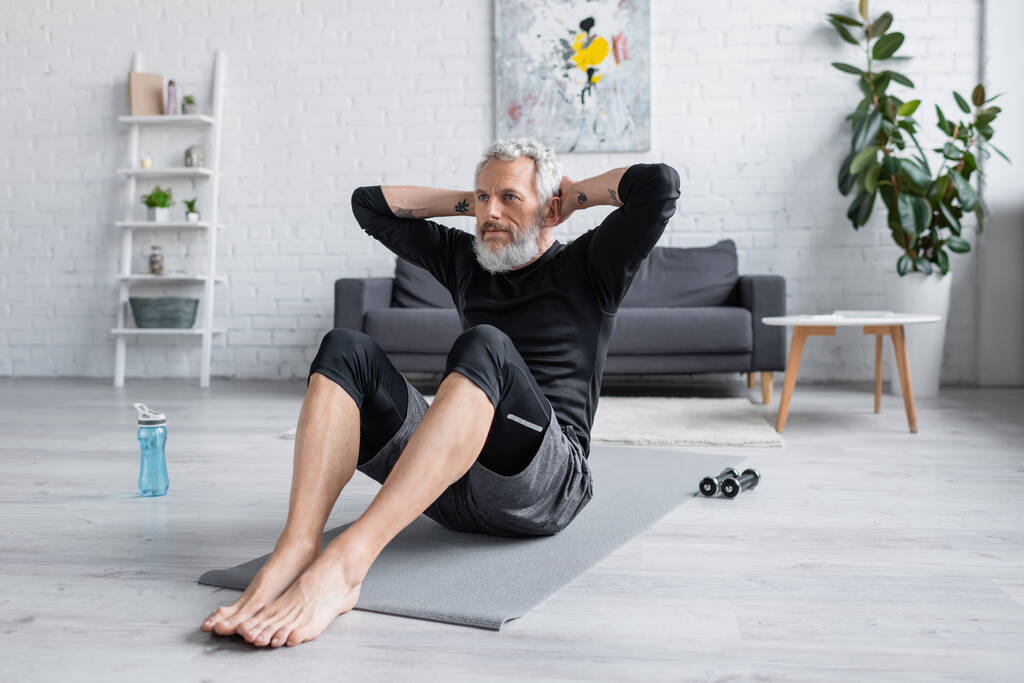 Barfuß-Mann trainiert auf Fitnessmatte im modernen Wohnzimmer - Foto, Bild