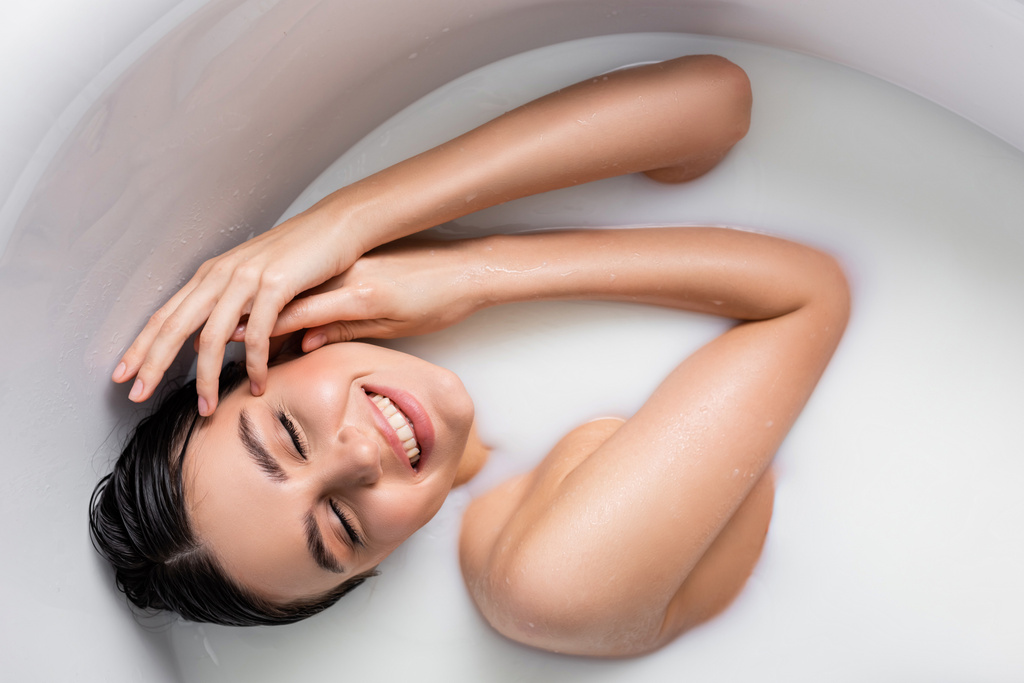 fiatal nő mosolyog csukott szemmel, miközben pihentető fürdőkádban tejjel - Fotó, kép