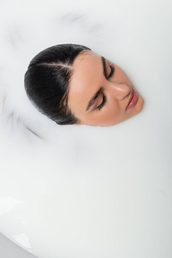 Ansicht einer Frau mit geschlossenen Augen, die ein Milchbad nimmt - Foto, Bild