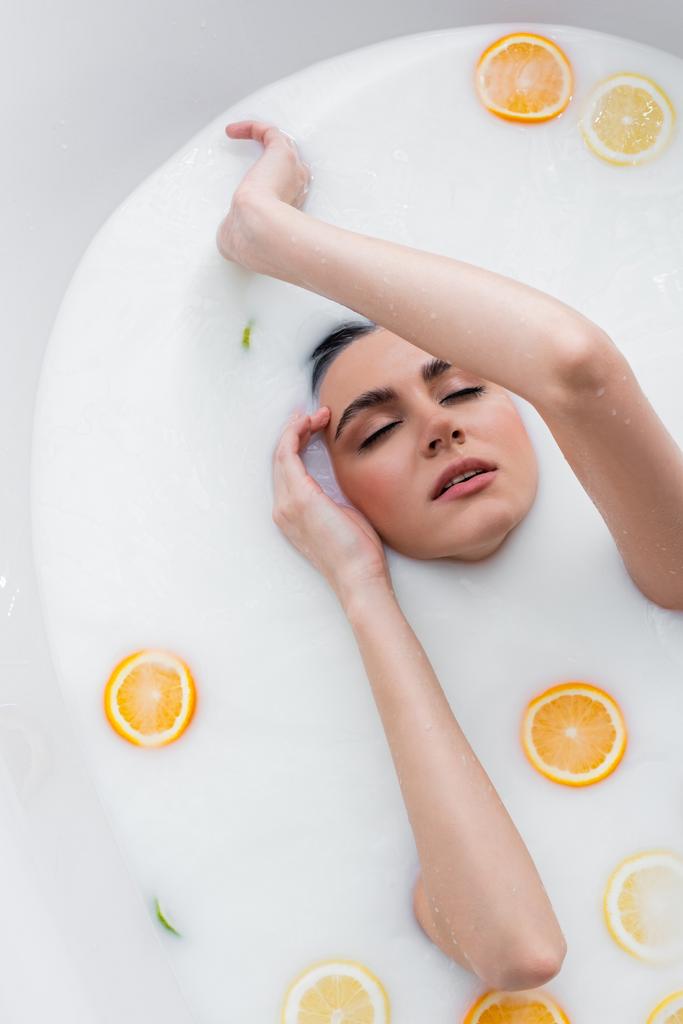 felső nézet a nő csukott szemmel fürdés tejben szeletelt citrusszal - Fotó, kép