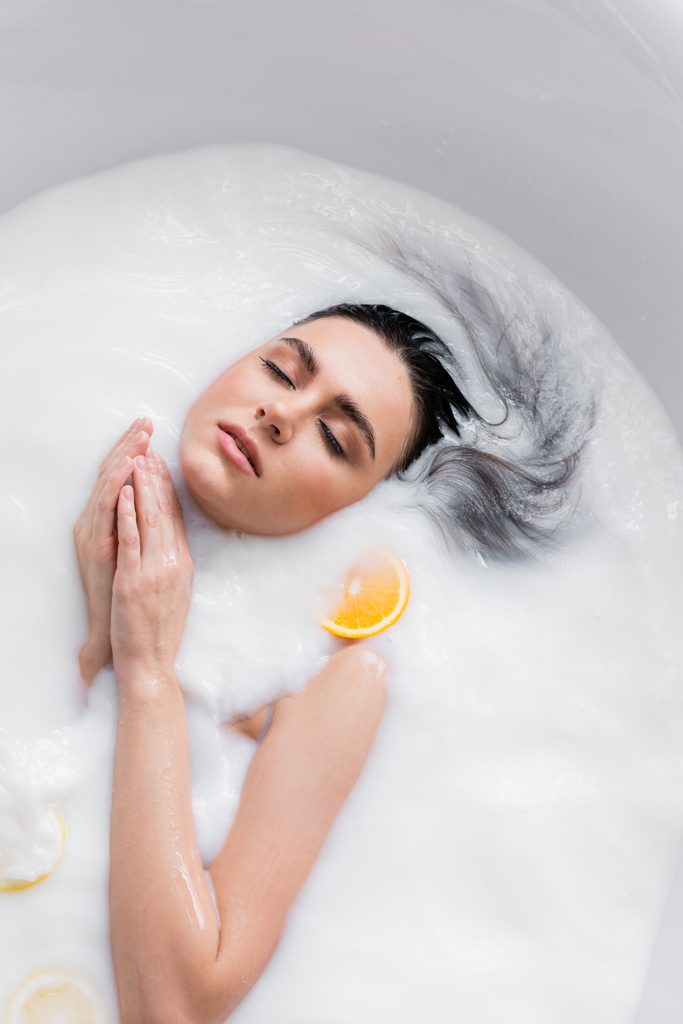 bonita joven bañándose en leche con rodajas de limón y naranja - Foto, Imagen