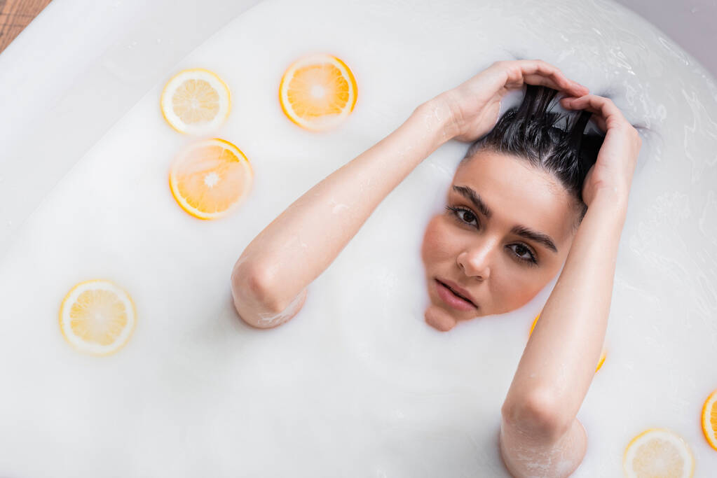 młoda kobieta patrząc w aparat podczas kąpieli mlecznej ze świeżymi owocami cytrusowymi - Zdjęcie, obraz