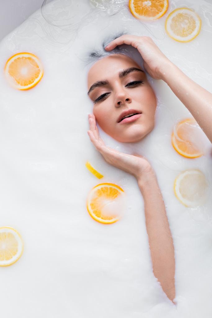 手の近くにいる若い女性が柑橘系のスライスとミルク風呂でリラックス - 写真・画像
