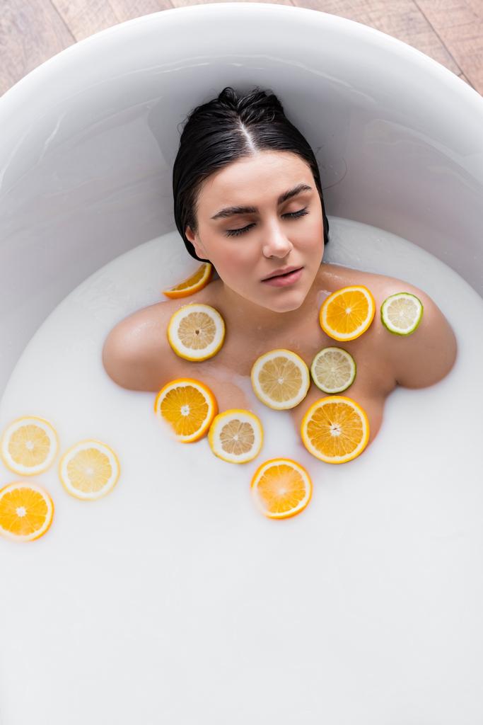 overhead view of young woman in milky bath with fresh citrus slices - Photo, Image