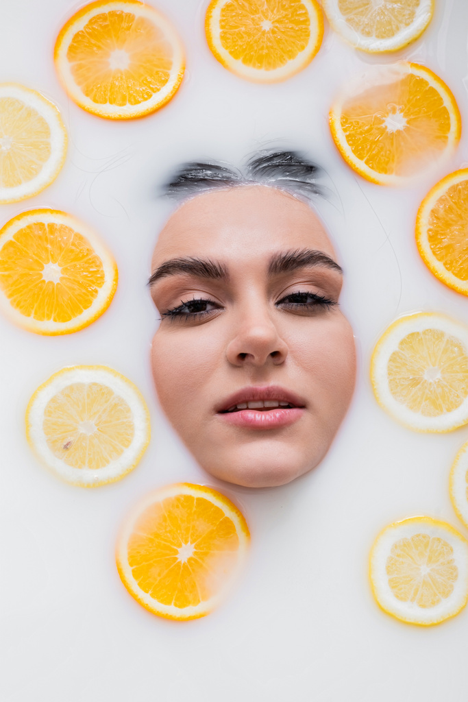 vista dall'alto del viso femminile nel bagno lattiginoso con limoni e arance tagliati a fette - Foto, immagini