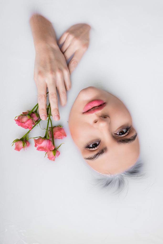 top view of woman looking at camera while bathing in milk with pink roses - Photo, Image