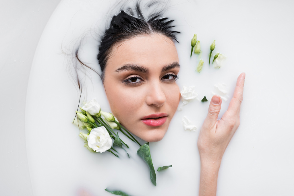 mulher sensual olhando para a câmera enquanto toma banho de leite com flores eustoma - Foto, Imagem
