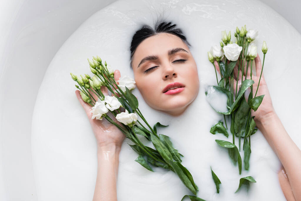 fiatal nő csukott szemmel élvezi fürdés tejben eustoma virágok - Fotó, kép