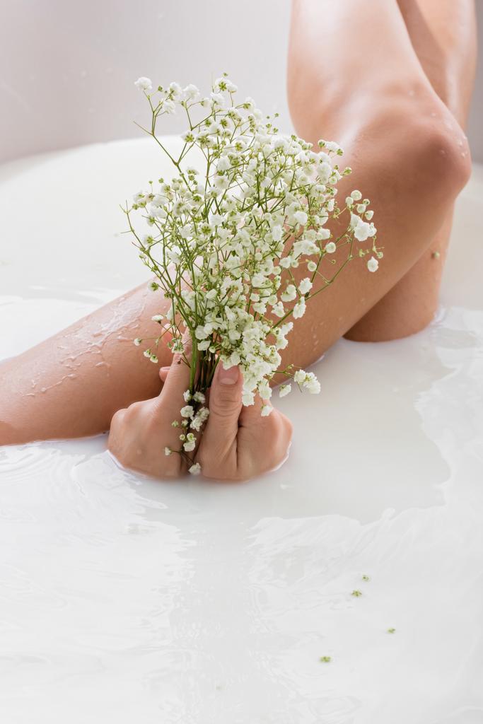 partial view of woman holding white, tiny flowers while enjoying milk bath - Photo, Image