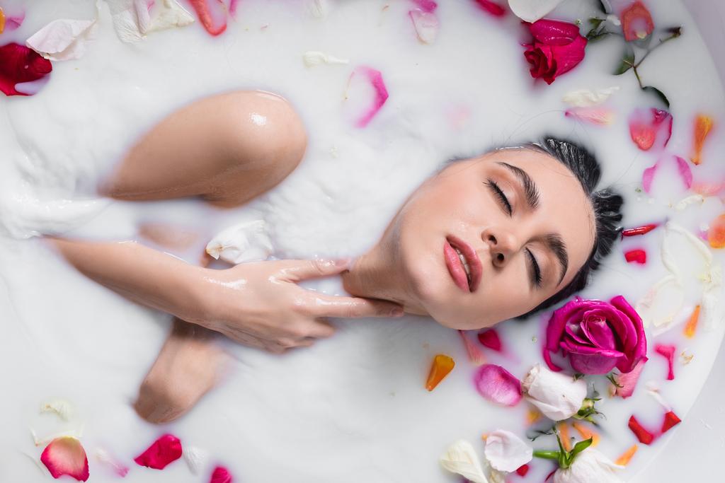 sensuele vrouw aanraken hals tijdens het nemen van melk bad met rozenblaadjes - Foto, afbeelding