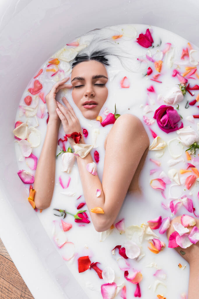 молодая женщина с закрытыми глазами наслаждается цветочной ванной с молоком - Фото, изображение