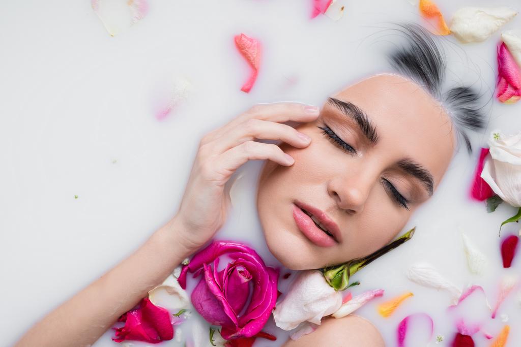 sensual woman touching face while taking milk bath with rose petals - Photo, Image