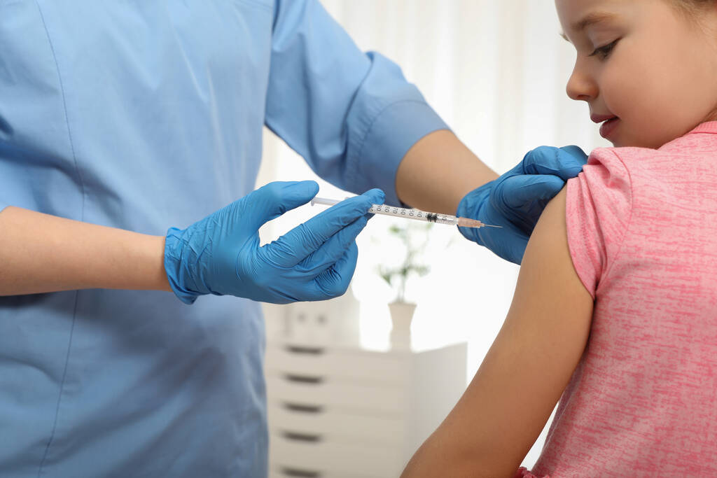 Dokter die een injectie geeft aan een klein meisje in het ziekenhuis. Inentingsconcept - Foto, afbeelding