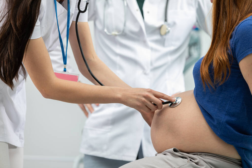 Vista de cerca de una doctora auscultando el abdomen de una mujer embarazada con un estetoscopio. Oficina de médicos profesionales - Foto, imagen