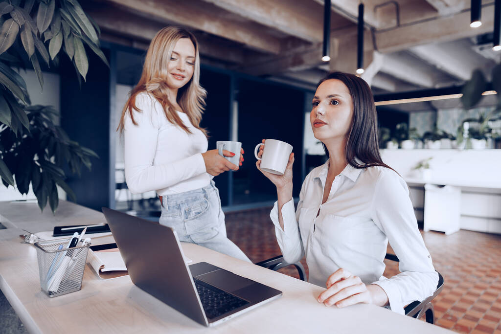 2人の若い女性同僚がオフィスでコーヒーを飲む - 写真・画像