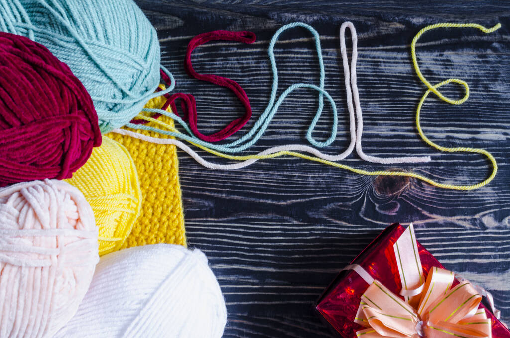 skeins of colored yarn and the word "Sale" of colored threads on a wooden background needlework concept sale on knitting products - Photo, Image