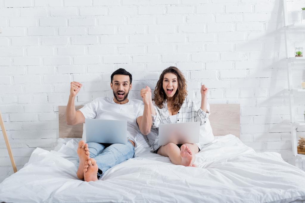 boldog többnemzetiségű szabadúszók fekszenek az ágyon laptopokkal  - Fotó, kép