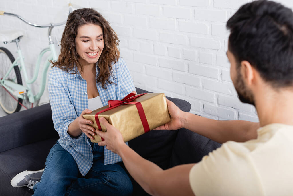 wazig moslim man geven verpakt cadeau aan gelukkig vriendin in woonkamer - Foto, afbeelding