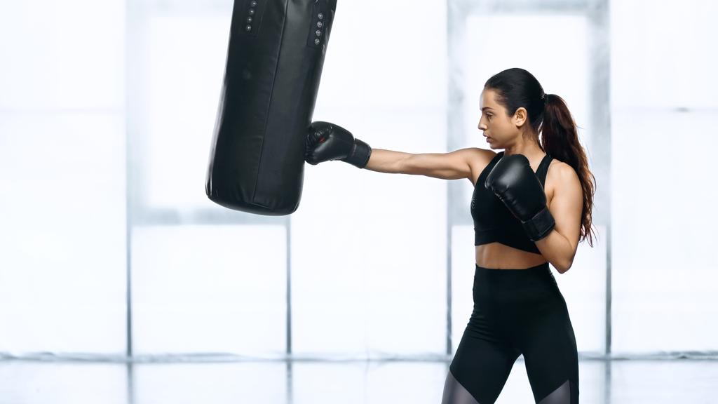 side view of focused sportswoman training with punching bag in gym  - Photo, Image