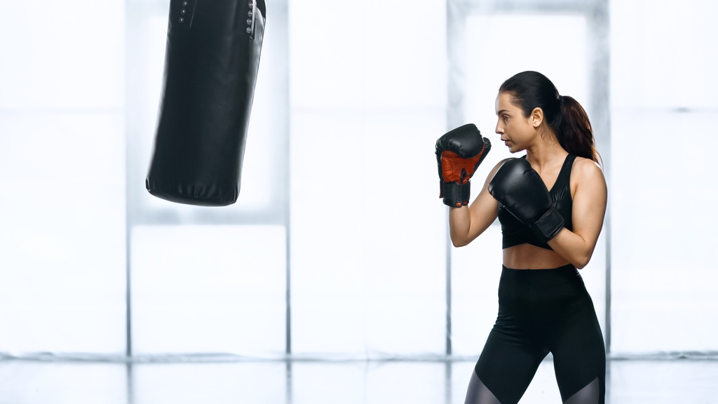 boční pohled na soustředěný ženský trénink s boxovací taškou v tělocvičně  - Fotografie, Obrázek