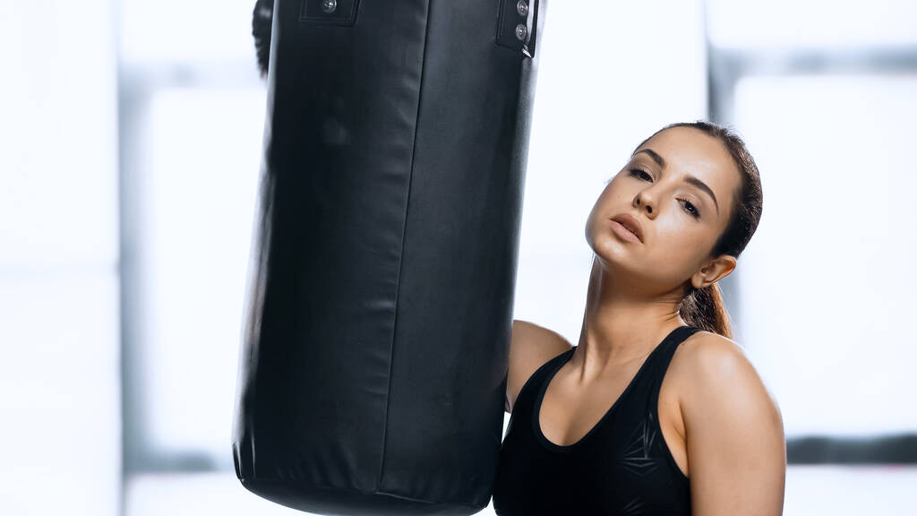 tired young woman in boxing glove resting near punching bag in gym  - Photo, Image