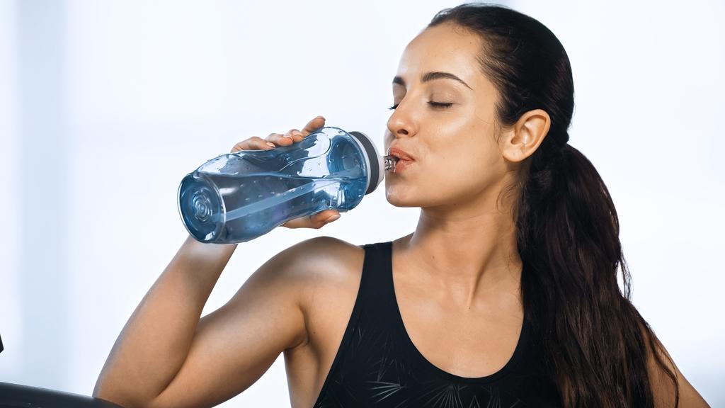 молода спортивна жінка тримає спортивну пляшку і питну воду в спортзалі
  - Фото, зображення