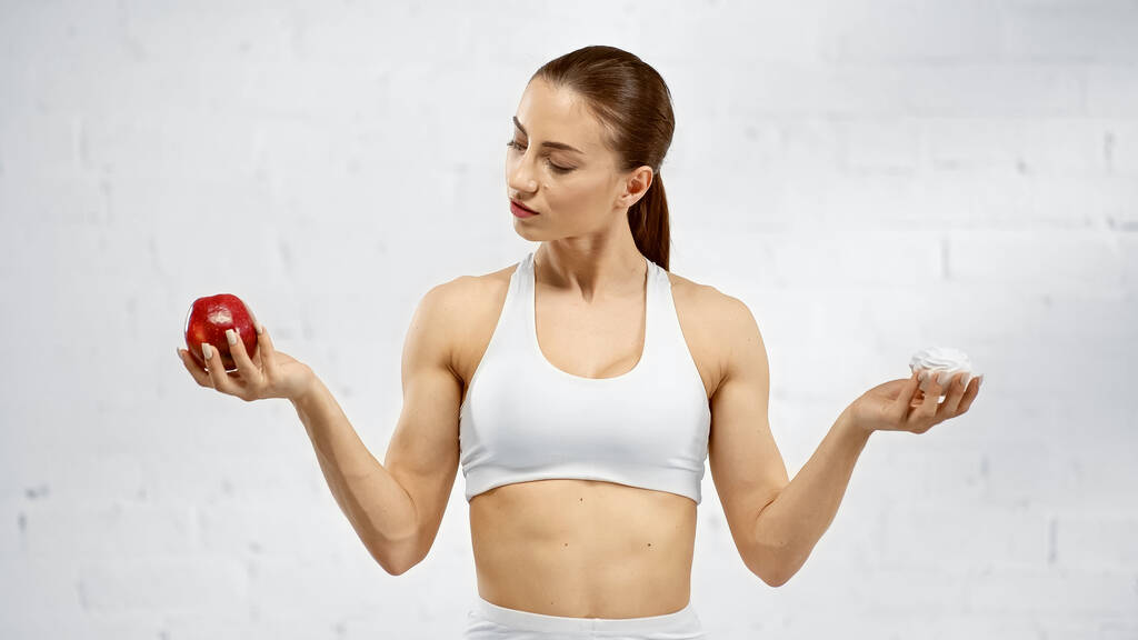 Молода спортсменка з яблуком і смачним зефіром біля білої стіни
  - Фото, зображення