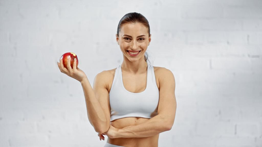 Esportista positivo segurando maçã e olhando para a câmera  - Foto, Imagem