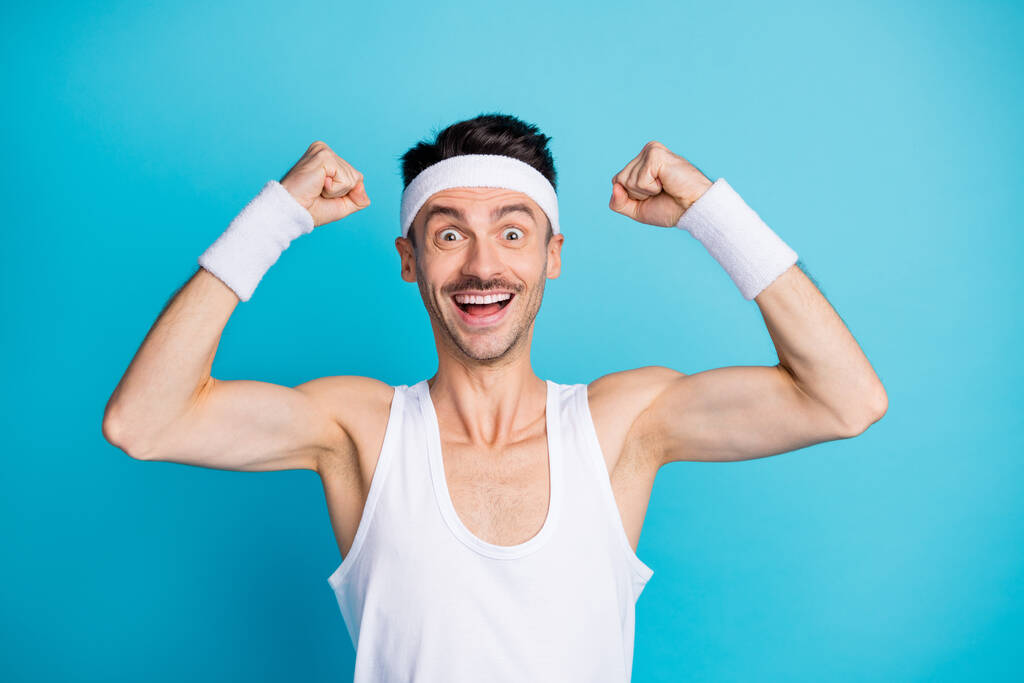 Photo de surprenant sportif homme montrer triceps muscles après résultat de gymnastique porter blanc débardeur singulet isolé sur fond de couleur bleue - Photo, image
