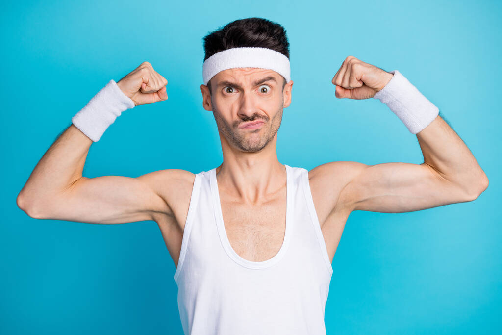 Kuva keskittynyt urheilullinen kaveri näyttää lihakset kädet kuluvat valkoinen säiliö-top singlet eristetty sininen väri tausta - Valokuva, kuva