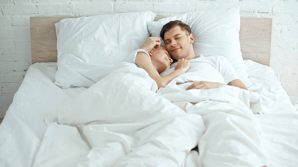 smiling young couple lying under blanket on bed - Photo, Image