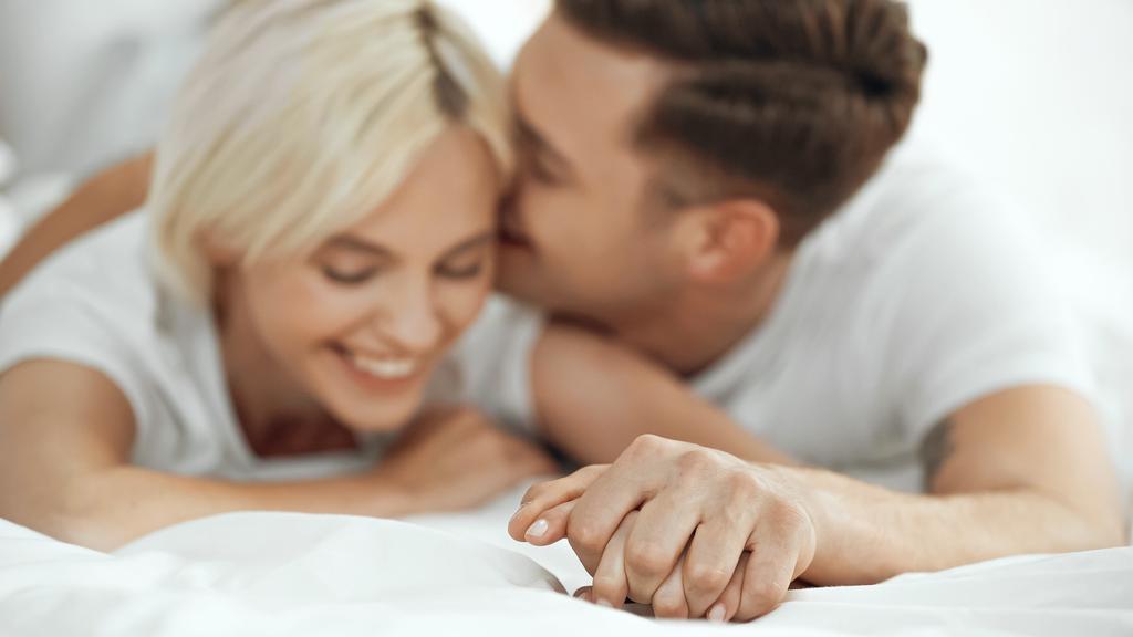 niewyraźna młoda kobieta i mężczyzna trzymający się za ręce i uśmiechający się w łóżku - Zdjęcie, obraz