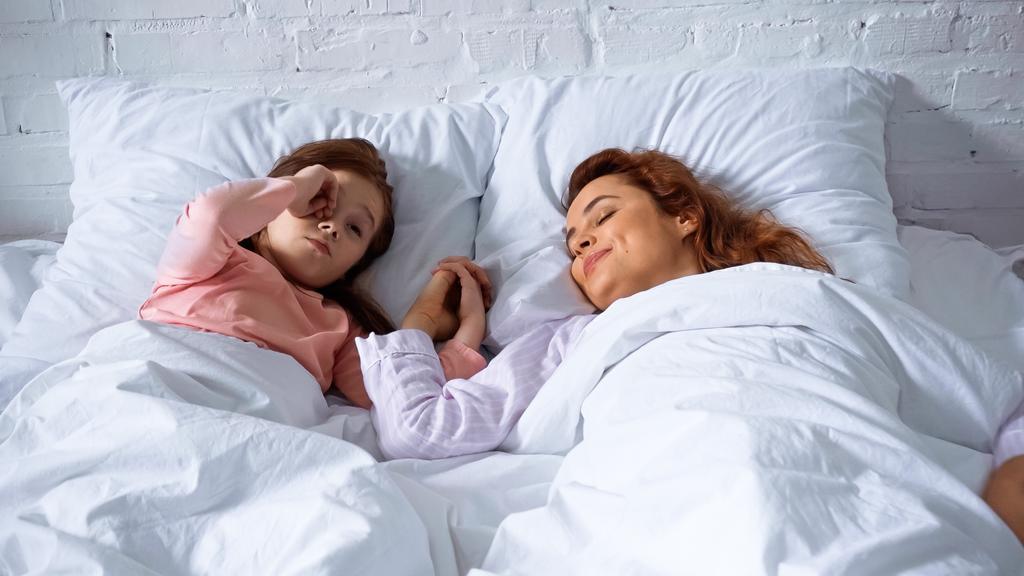 Sorridente madre e bambino che si tiene per mano sul letto  - Foto, immagini