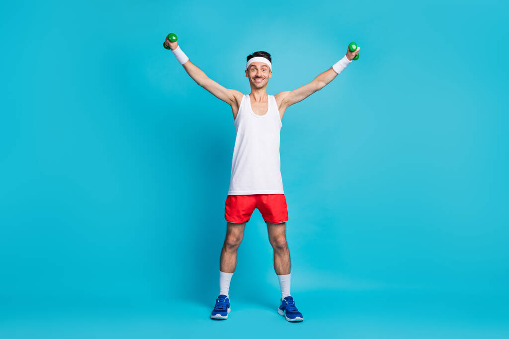 Pełna długość zdjęcie młodego sportowca szczęśliwy pozytywny uśmiech zrobić ćwiczenia fizyczne z małych sztangi izolowane nad niebieskim tle kolor - Zdjęcie, obraz