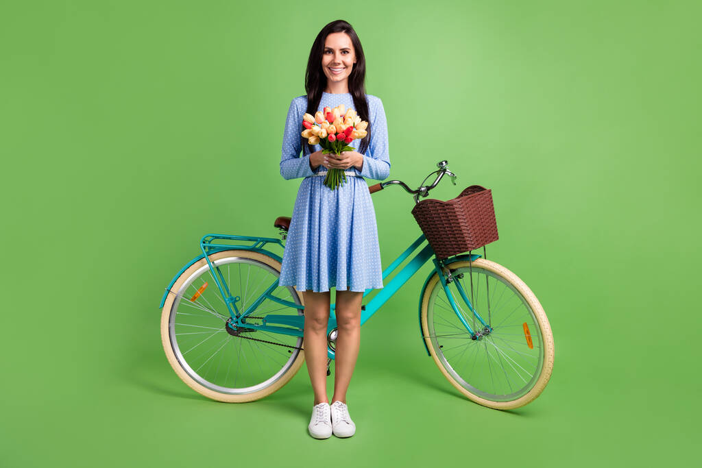 Foto de linda encantadora joven vestida con traje azul sosteniendo ramo de bicicleta sonriendo aislado color verde fondo - Foto, Imagen