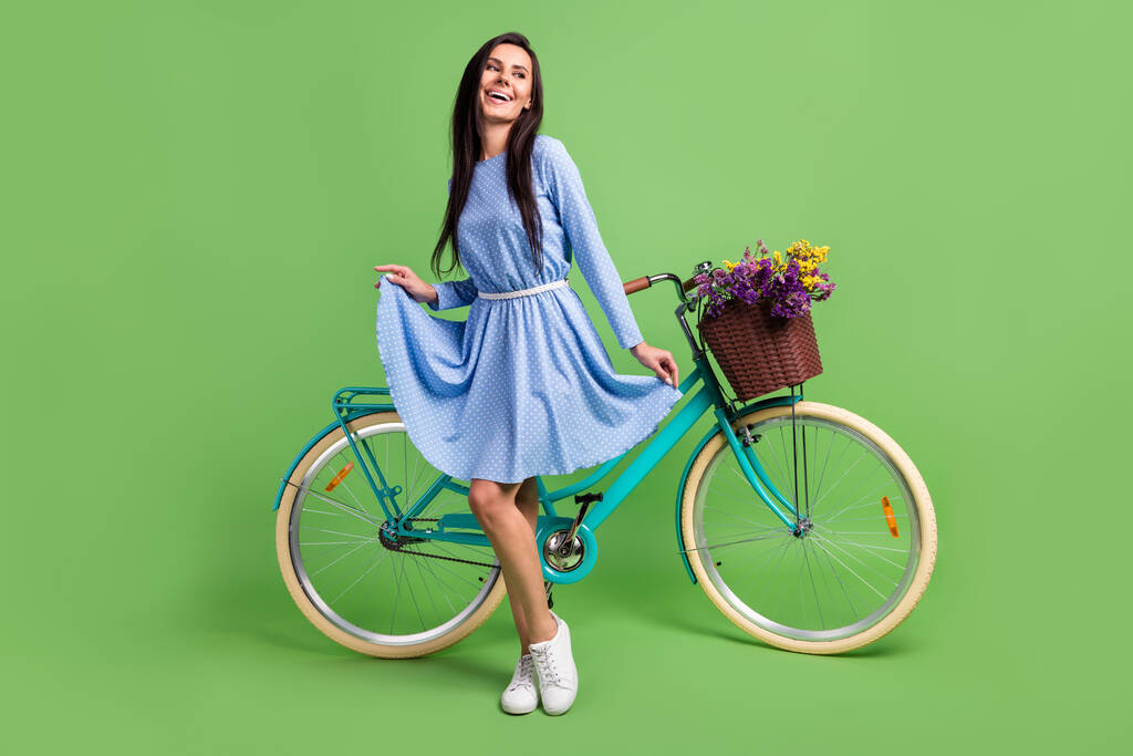 Foto di carino graziosa signora indossare vestiti punteggiati sorridente tenuta vestito gonna bicicletta cercando spazio vuoto isolato colore verde sfondo - Foto, immagini