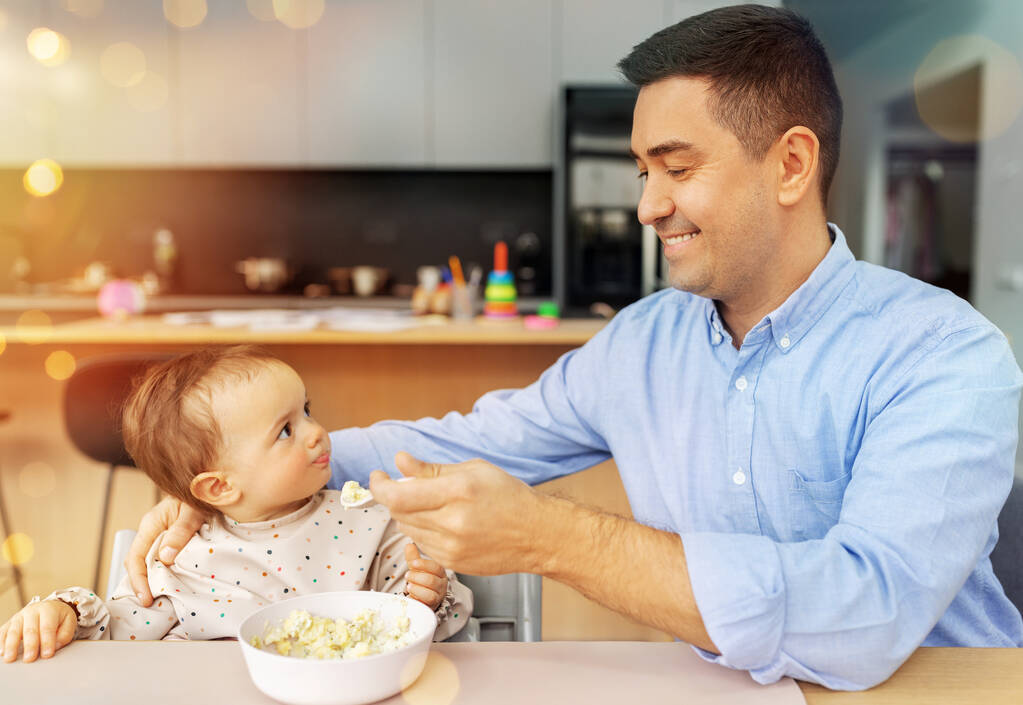 gelukkig vader voeden baby in kinderstoel thuis - Foto, afbeelding