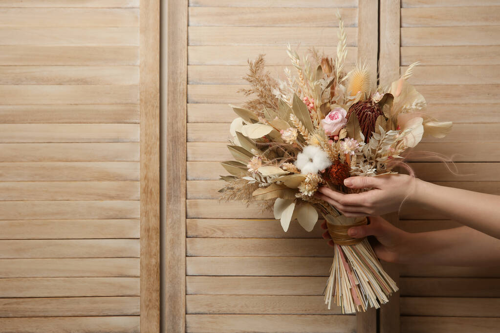 女性の木製の背景に美しいドライフラワー花束を保持、クローズアップ。テキストのスペース - 写真・画像