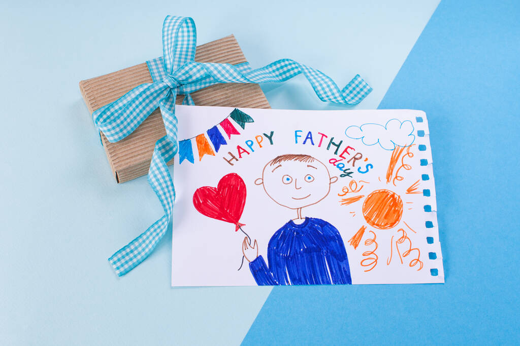 Happy Fathers Day. Childs drawing of her dad and gift a blue minimal background. - Photo, Image