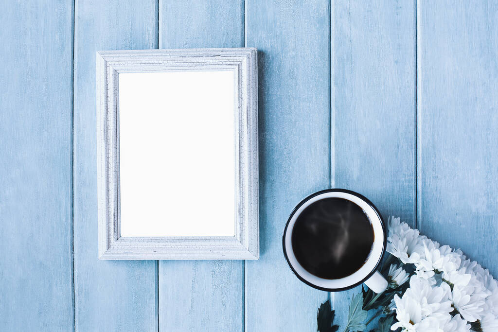 Blank vertical empty picture frame over blue rustic background with steaming coffee and white daisy flowers. - Photo, Image